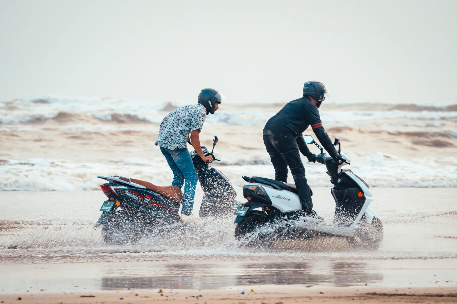 Two riders on Tunwal electric scooters along a beach